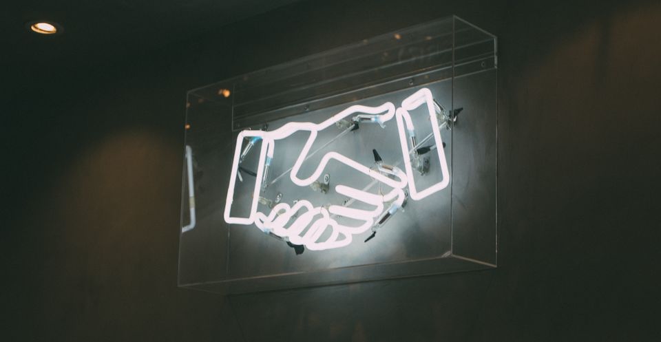 White neon sign with two hands shaking 